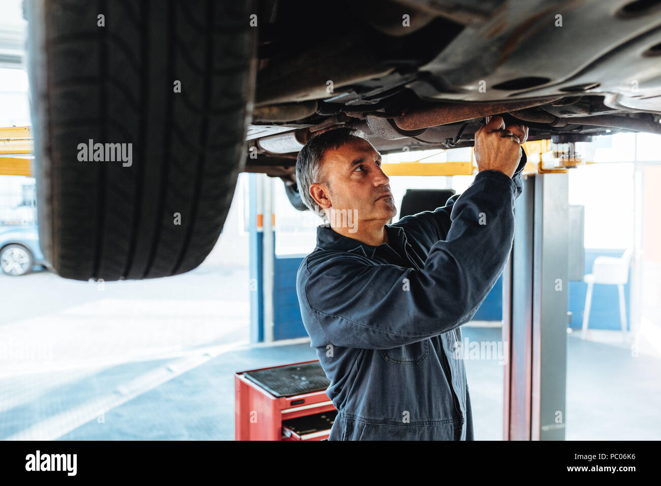 Mechaniker arbeitet an einer angehobenen Automobil an der Tankstelle. Erfahrene Reparatur Mann in seiner Garage arbeiten. Stockfoto