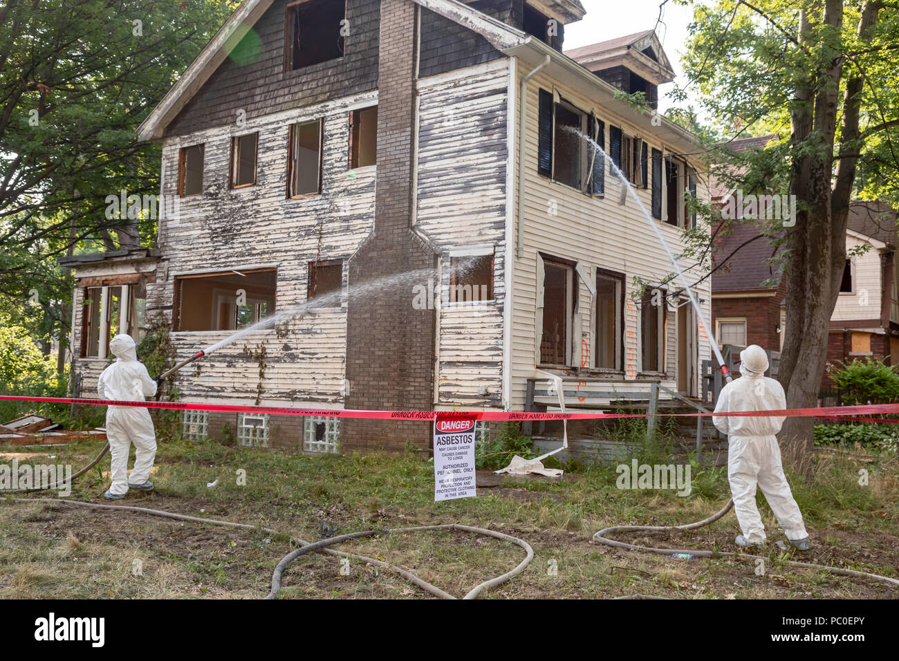 Detroit, Michigan - Verwendung von Schutzkleidung gegen Asbestexposition der Arbeitnehmer zu schützen, ein verlassenes Haus demolieren. Sie Wasser auf die buildin Stockfoto