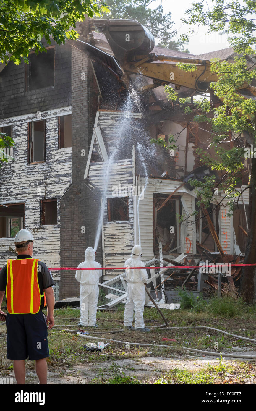 Detroit, Michigan - Verwendung von Schutzkleidung gegen Asbestexposition der Arbeitnehmer zu schützen, ein verlassenes Haus demolieren. Sie Wasser auf die buildin Stockfoto