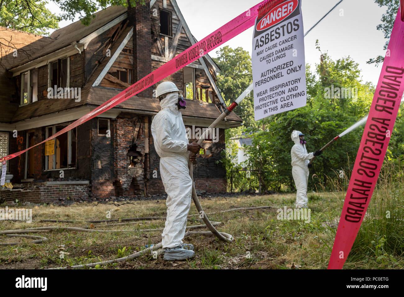 Detroit, Michigan - Verwendung von Schutzkleidung gegen Asbestexposition der Arbeitnehmer zu schützen, verlassene Häuser abzureißen. Sie Wasser auf die Gebäude Stockfoto