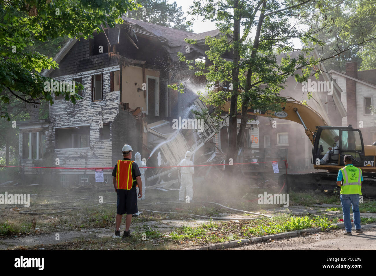 Detroit, Michigan - Staub hüllt eine Arbeitsstelle als Arbeitnehmer, mit Schutzkleidung gegen Asbestexposition zu bewachen, ein verlassenes Haus demolieren. Ein Stockfoto