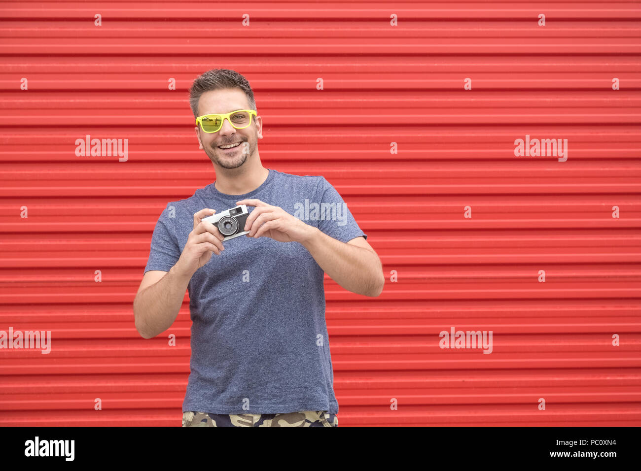 Portrait von hipster guy Holding vintage Kamera auf roten Hintergrund. Stockfoto