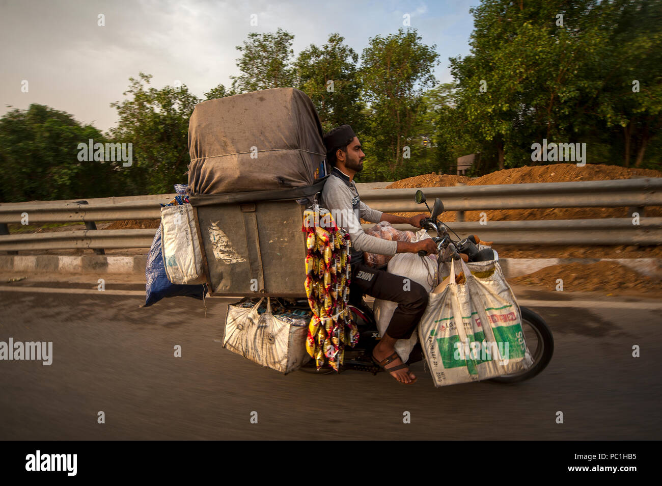 Indische Mann, der einen Haufen Dinge in seinem Motorrad, Neu Delhi, Indien Stockfoto