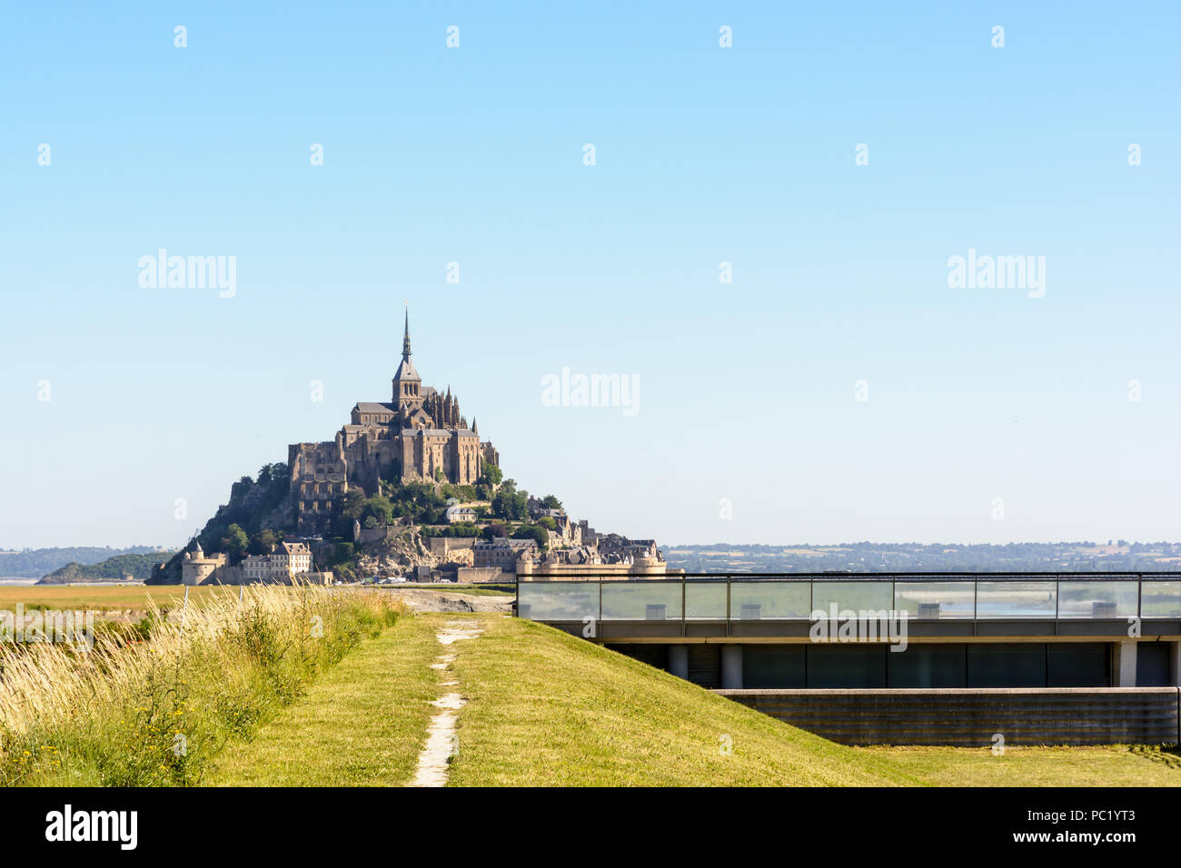 Blick auf den Mont Saint-Michel tidal Island in der Normandie, Frankreich, mit dem Damm auf der Couesnon river und ein Weg entlang des Flusses in den Vordergrund. Stockfoto