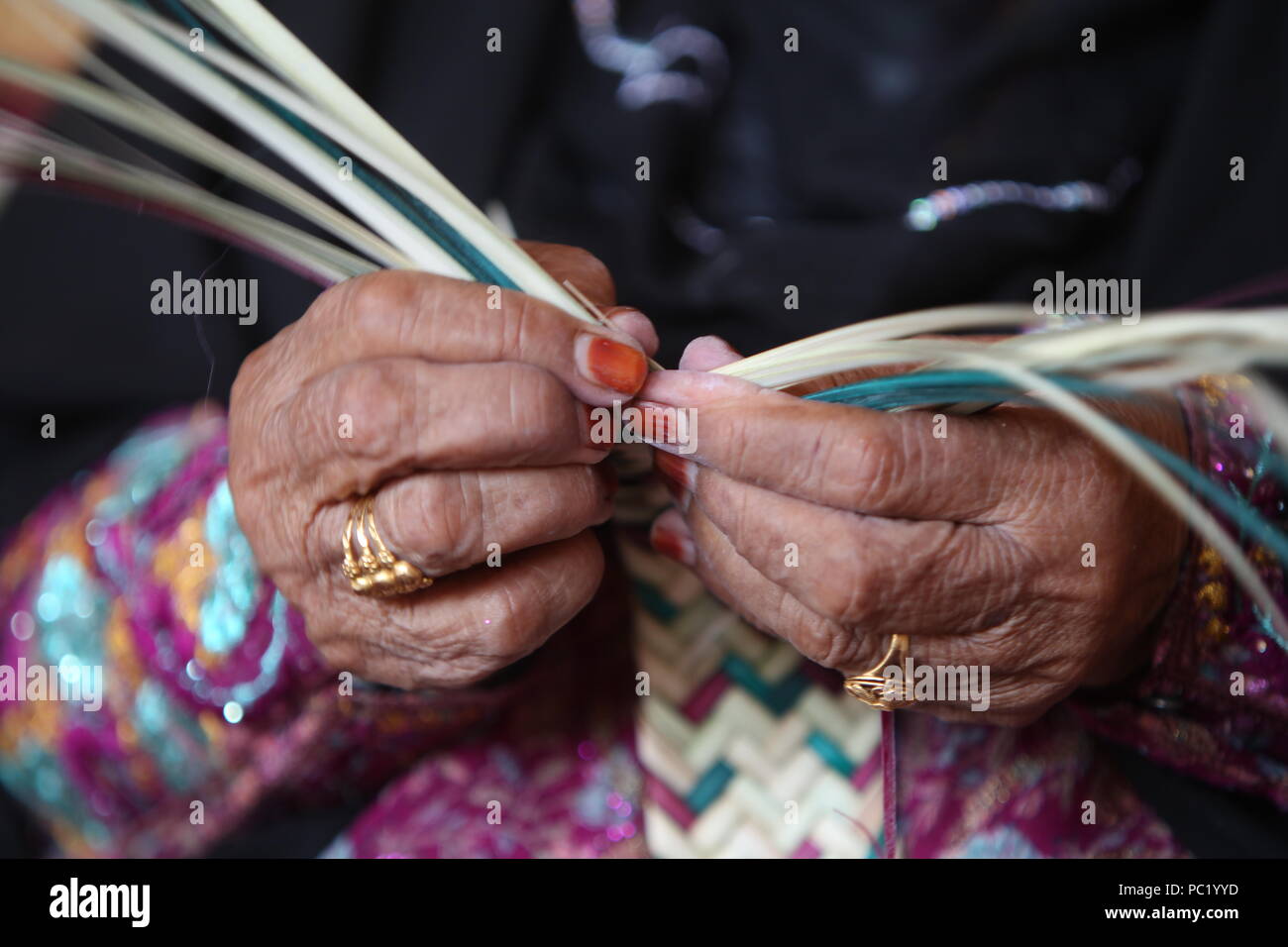 UAE Frau, sporting ein metallisches Burka mit Henna starb Finger, flicht Stroh Körbe und Matten aus Palmblättern im Heritage Village in Fujairah. Stockfoto
