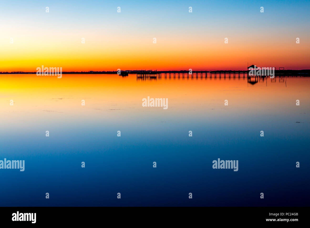 Eine mehrfarbige Sonnenuntergang alpenglow und seine Reflexion baden die Currituck Sound, und Silhouette Horizont-Pavillon und Promenade, Outer Banks, NC Stockfoto