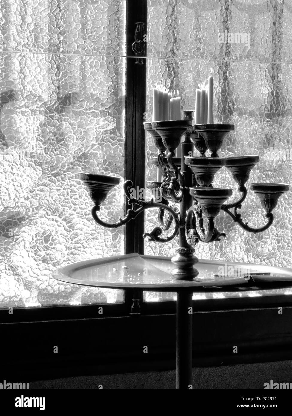 Schwarz-weiß Foto von alten Kronleuchter aus Europäischer Kirche mit Wachs Kerzen brennen hinter einem Fenster Stockfoto