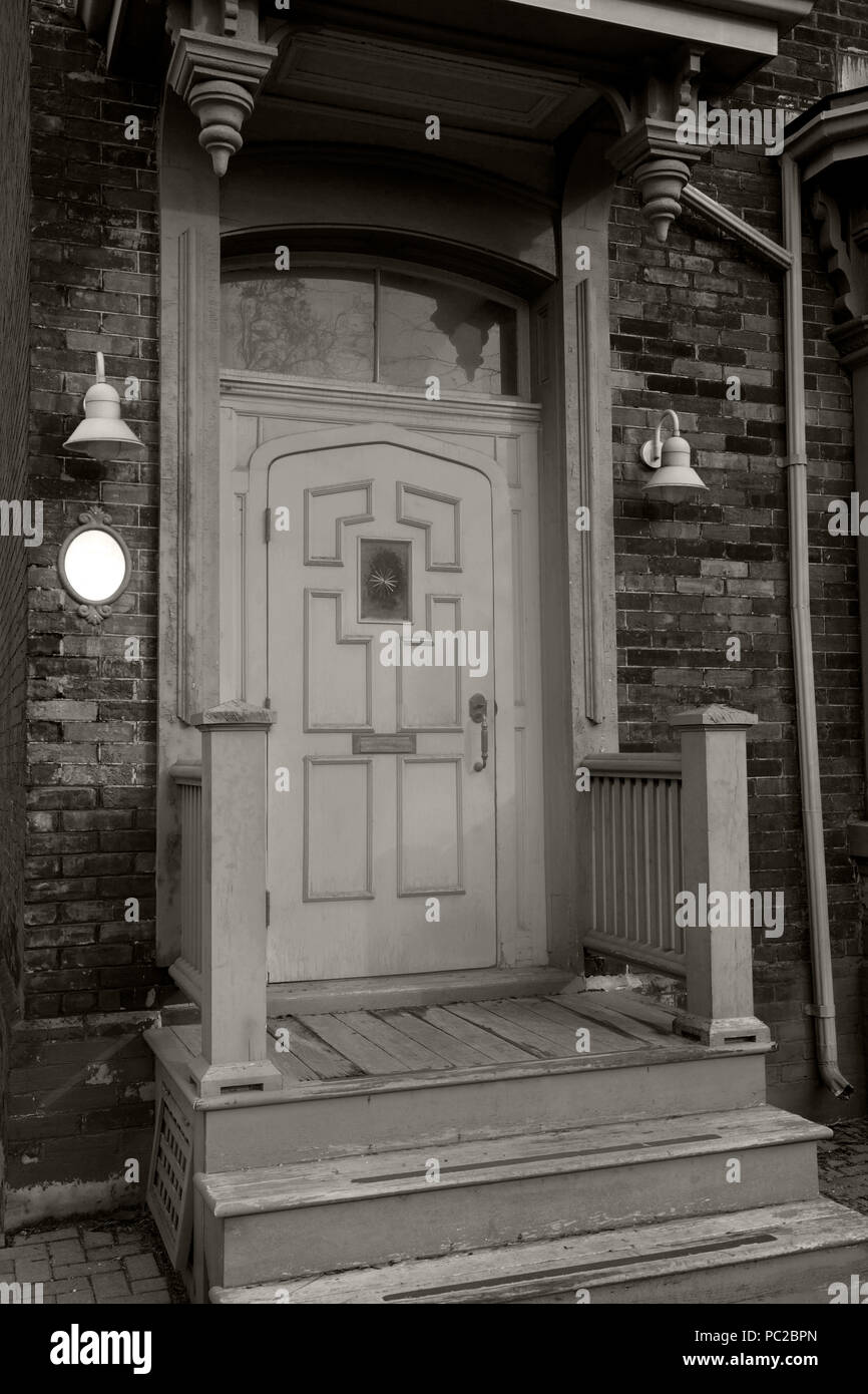Schwarz-Weiß-Foto einer Holztür vorne und eines Hauses aus Backstein in Kanada Stockfoto
