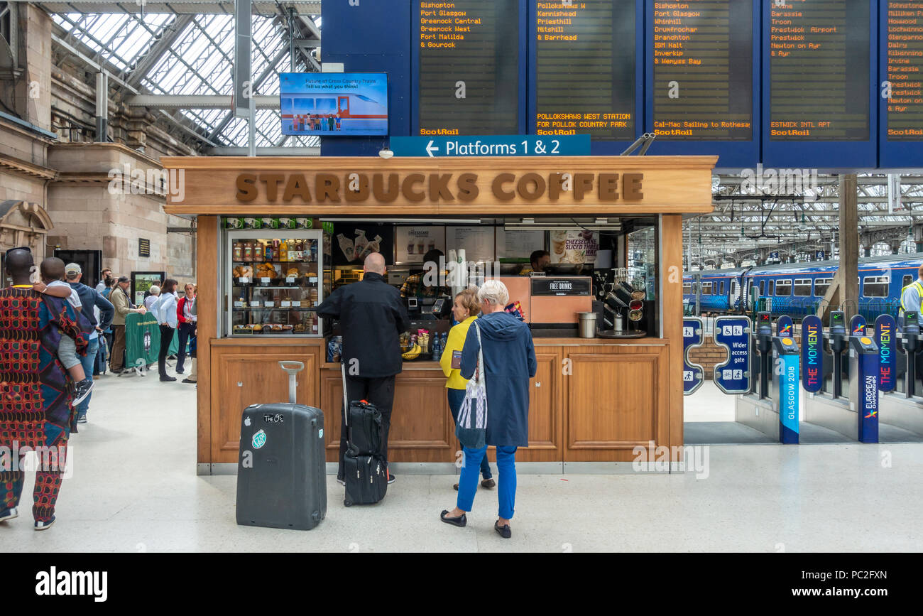 Baristas und Kunden im Starbucks Filiale in Glasgow Central Station. Passagiere in der Warteschlange für Zug. Abflüge. Ticket Barrieren. Stockfoto