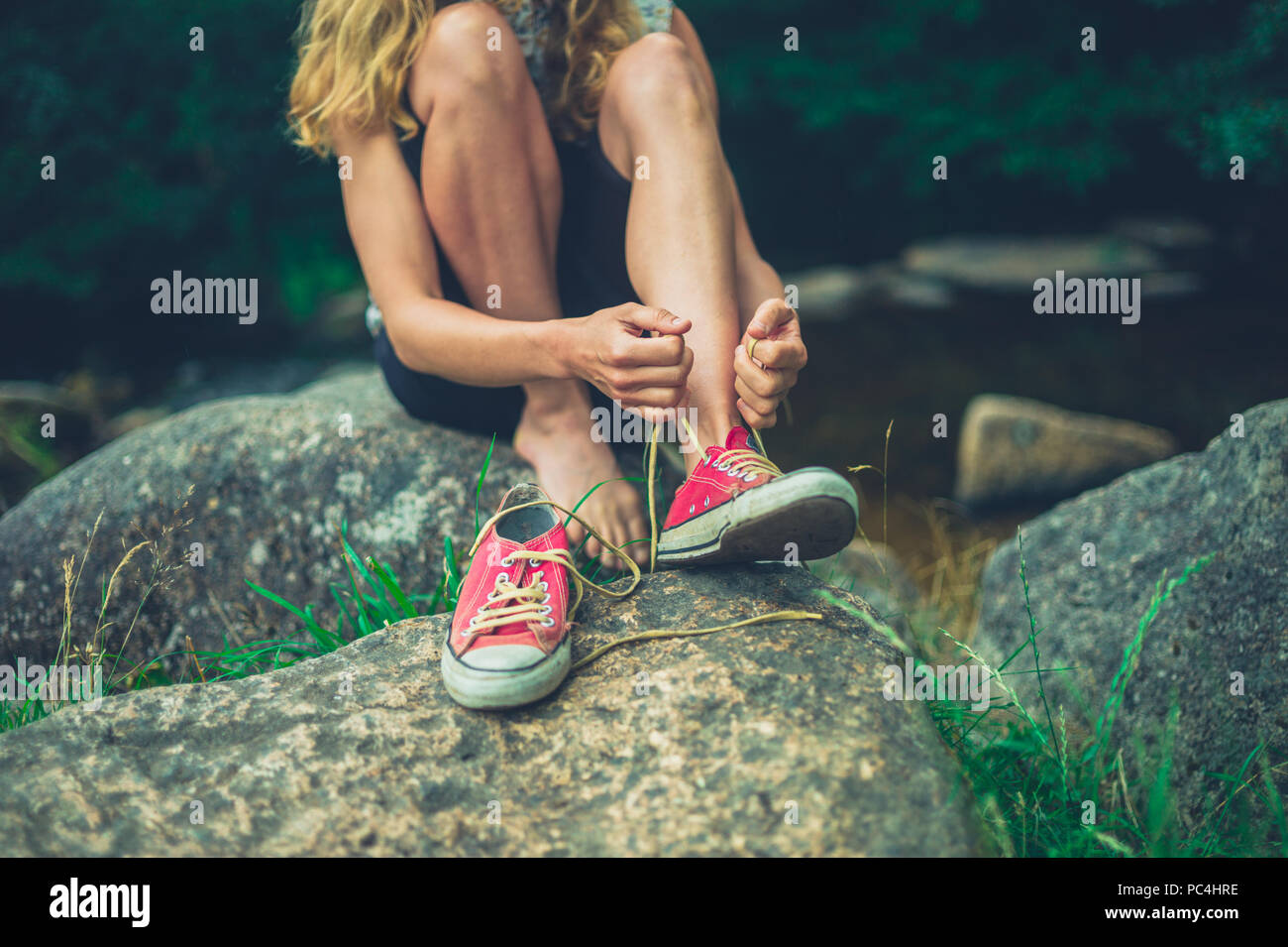 Eine junge Frau wird ihre Schuhe binden durch einen Fluss Stockfoto