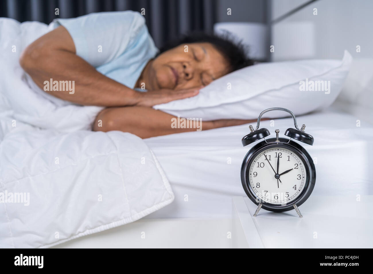 Ältere Frau schlafen in einem Bett mit einer Uhr Stockfoto