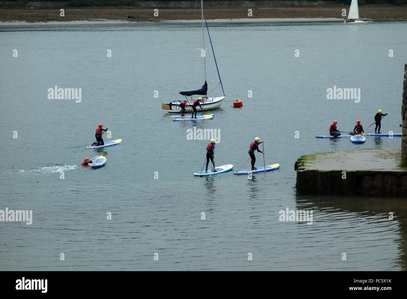 Kinder in Wetsuits auf Paddle Boards an ruhigen Gewässern im Menai Straits, zwischen Anglesey & Wales, UK. Stockfoto