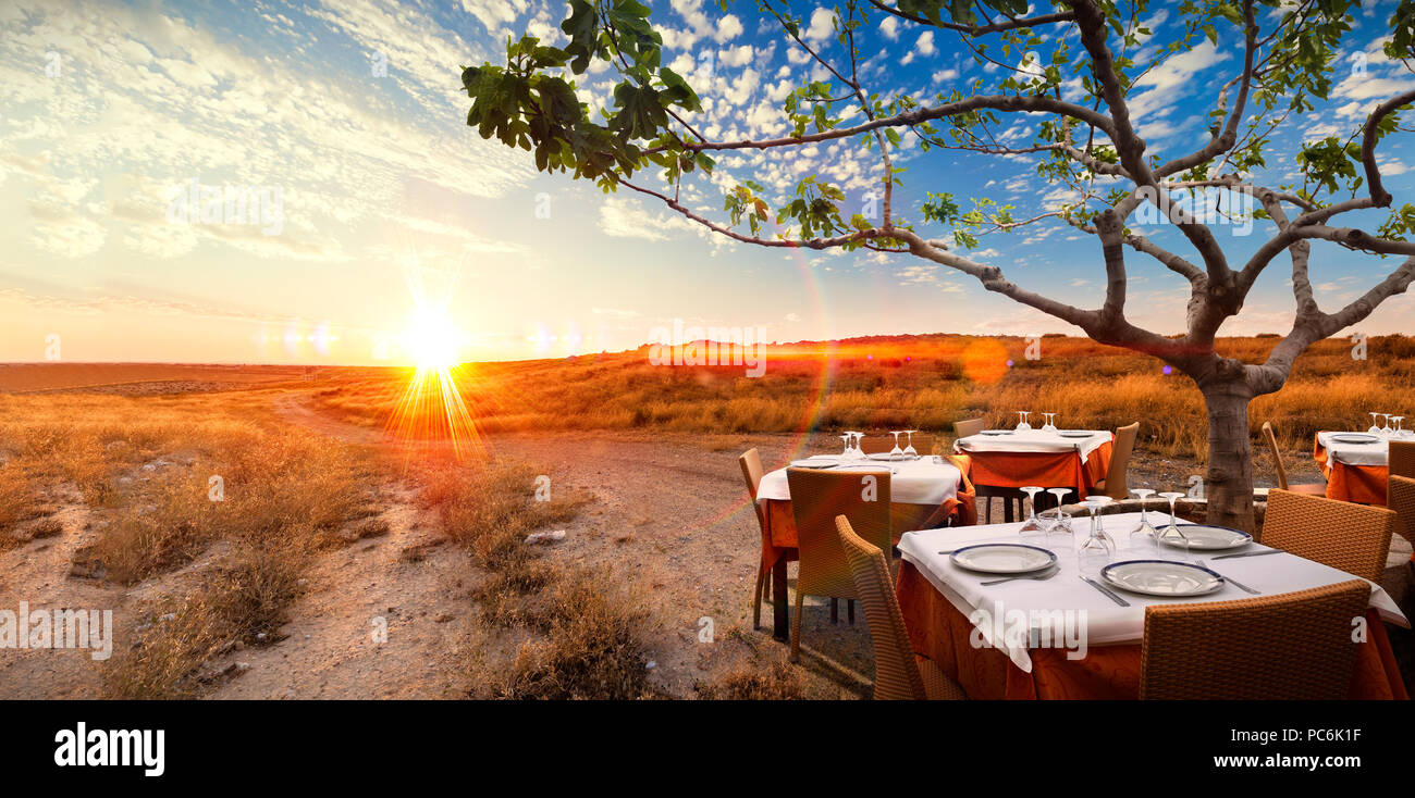 Surreale sunset Landschaft mit Tisch mit Speisen in romantische und idyllische Natur. Konzept der Gourmet und im Restaurant zu essen. Stockfoto