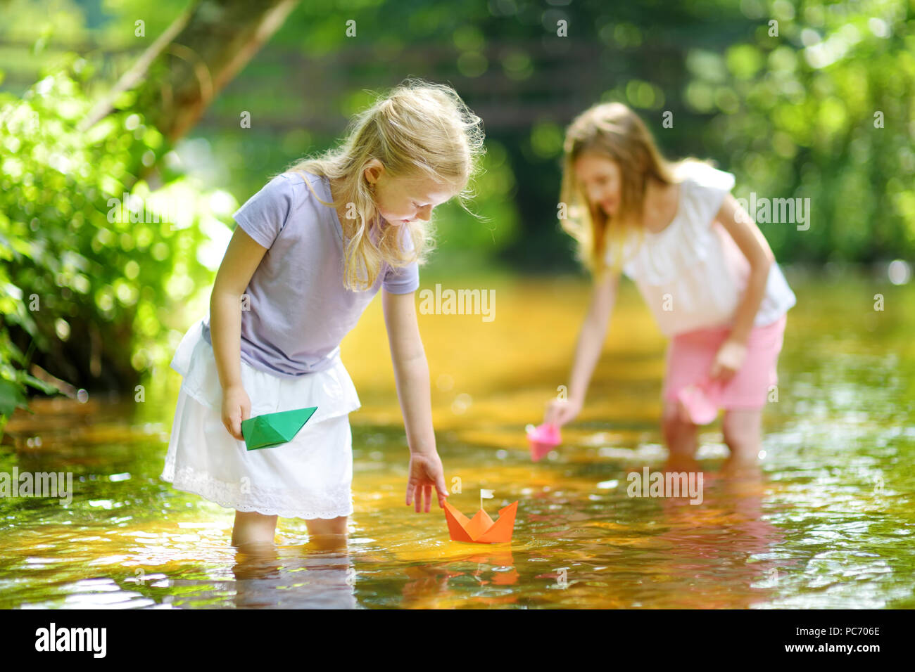 Zwei kleine Schwestern spielen mit Papier Boote durch einen Fluss an warmen und sonnigen Sommer. Kinder Spaß am Wasser. Aktivitäten im Sommer für kleine Zicklein Stockfoto