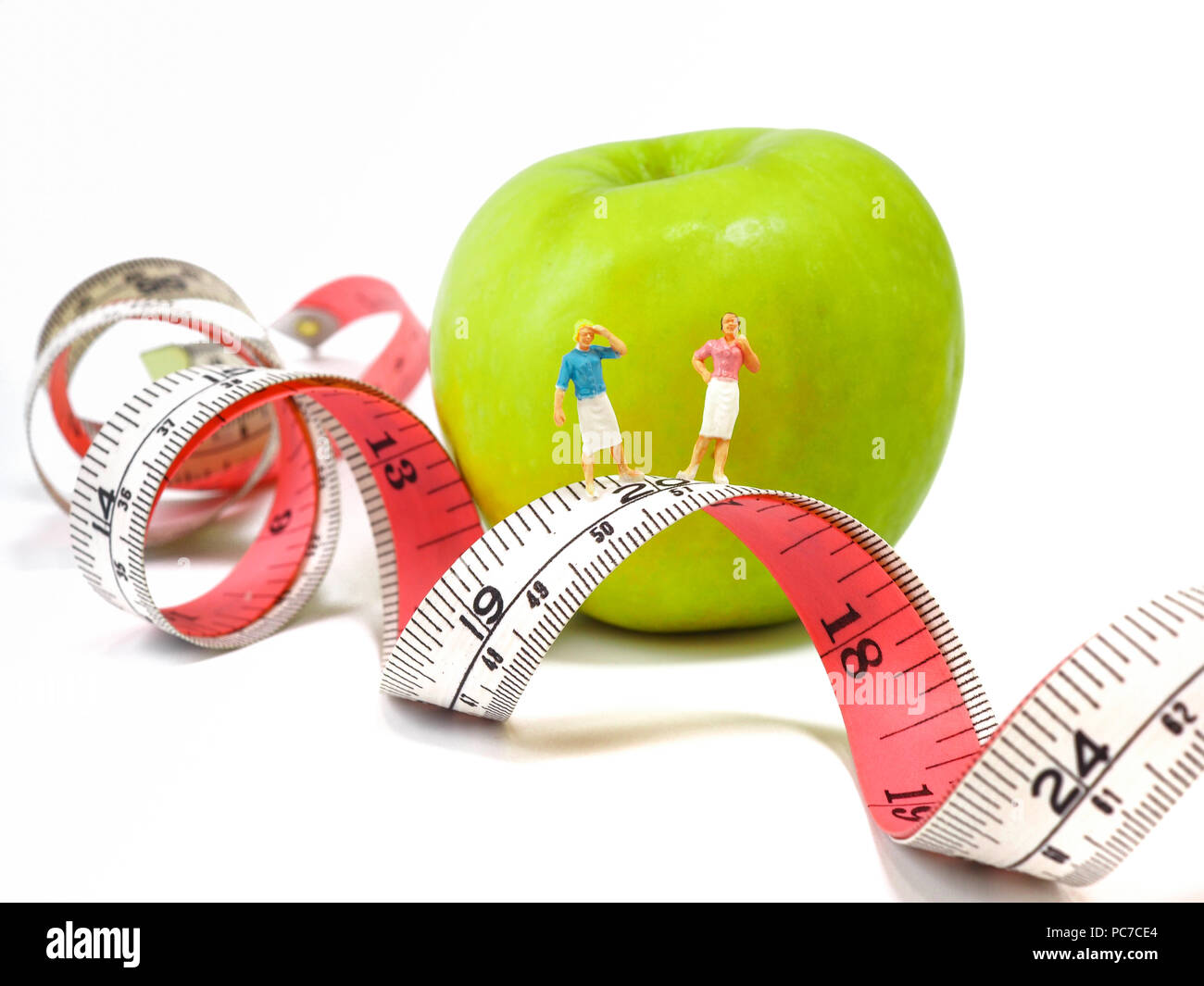 Miniatur Frau nahe Maßband und frisches Grün Apple stehen, Denken von Gewichtsverlust und schlanken Körper. Gesunder Lebensstil Konzept. Stockfoto
