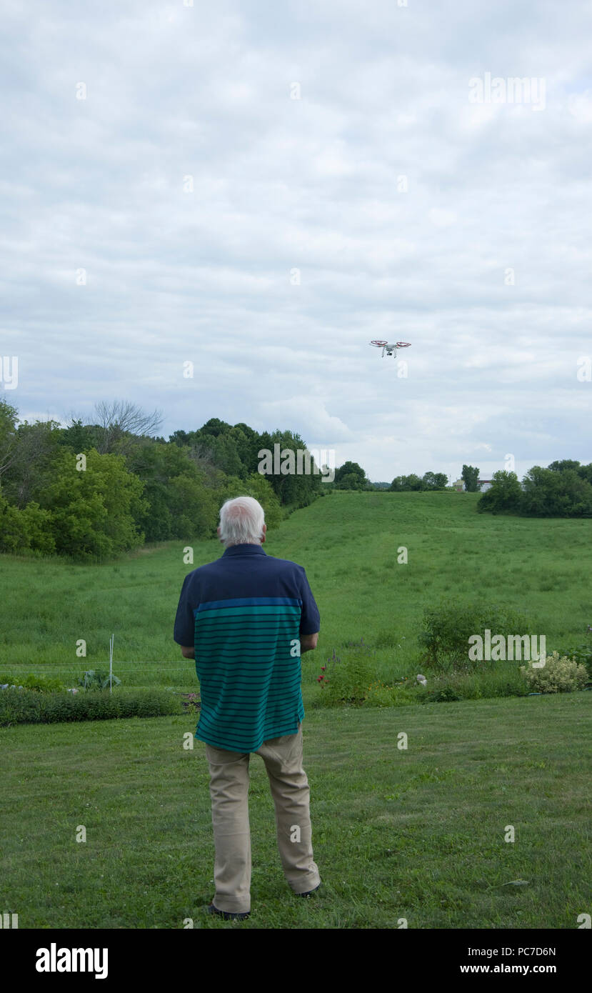 Mann Betrieb eines dji Phantom Quadcopter Drone unbemannte Luftfahrzeuge im Flug über offenes Feld. Stockfoto