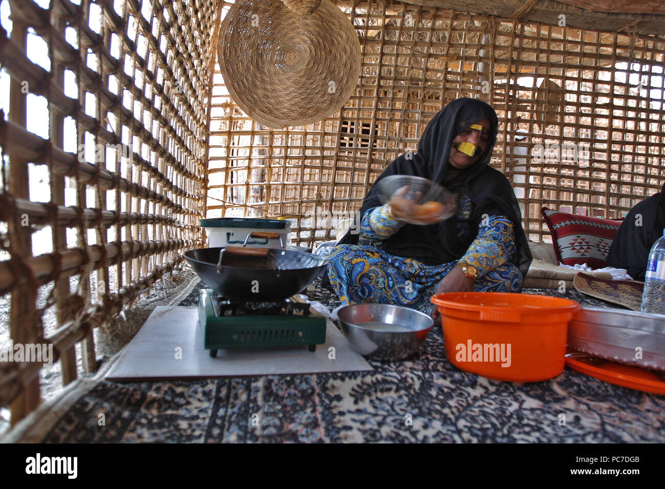 Eine Frau, sporting ein metallisches Burka, Köche Süßigkeiten zu ihrer Hütte im Heritage Village in den Vereinigten Arabischen Emiraten Fujairah. Stockfoto