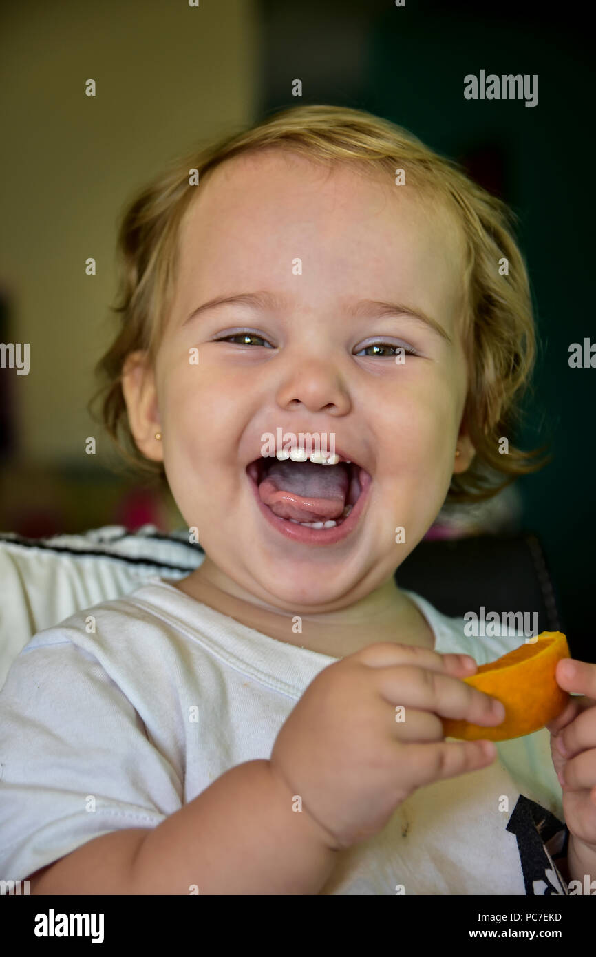 Baby Mädchen essen Orange zum ersten Mal. Zeigen Sie Ihr lustige Reaktionen während sie Geschmack der Frucht. Stockfoto
