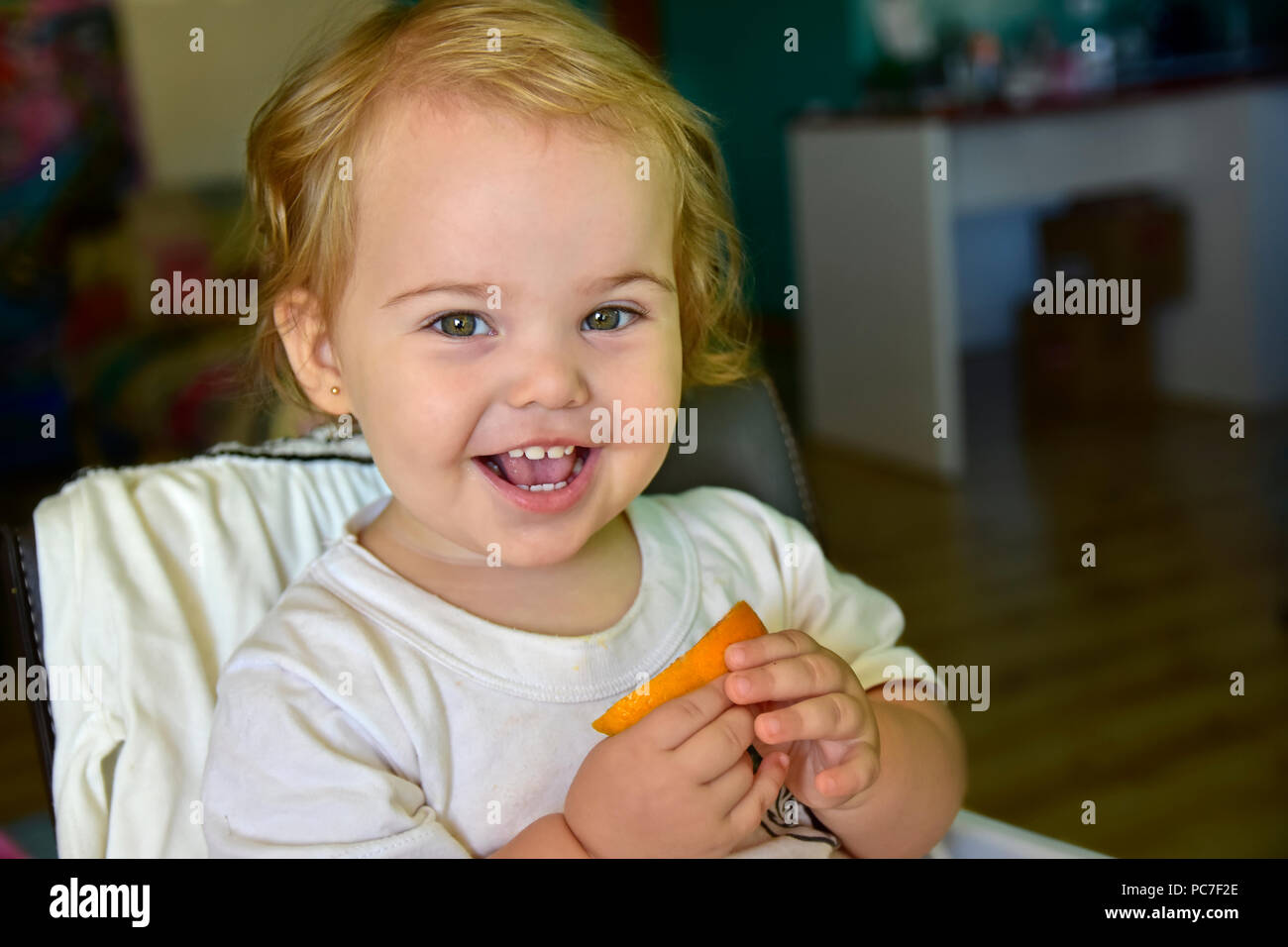 Baby Mädchen essen Orange zum ersten Mal. Zeigen Sie Ihr lustige Reaktionen während sie Geschmack der Frucht. Stockfoto
