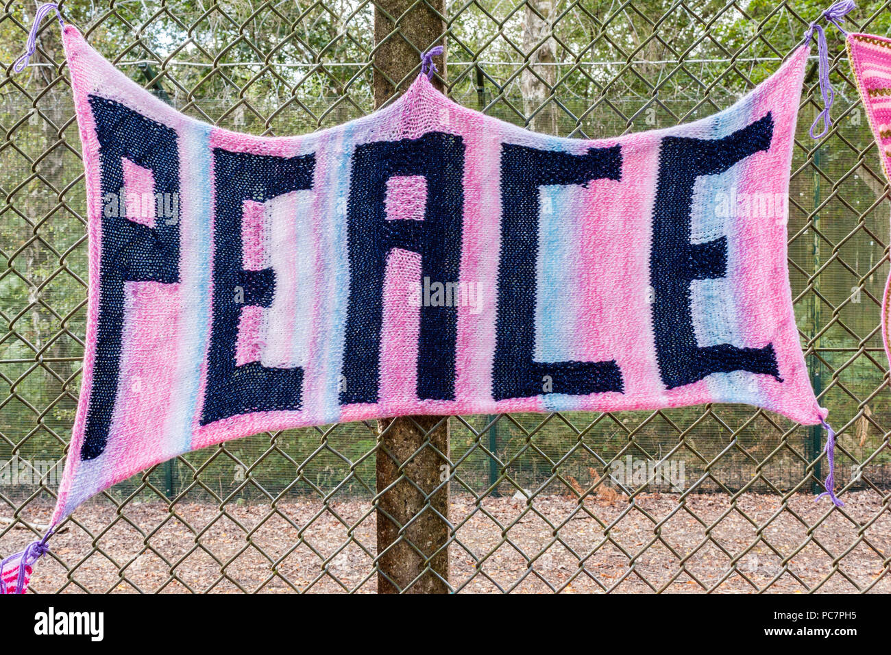 Strickschal mit das Wort 'Frieden' zu einem Zaun am Rand des Atomic Weapons Establishment in Aldermaston, Berkshire, England, GB gebunden. Stockfoto
