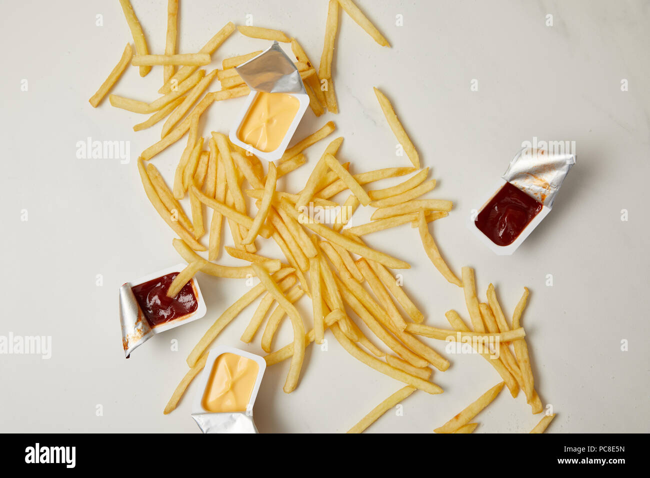 Blick von oben auf die Pommes Frites mit Behältern von Saucen auf Weiß Stockfoto