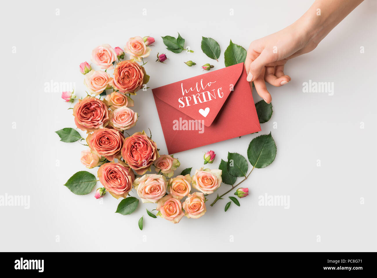 Hand mit Umschlag mit Hallo Frühling Schriftzug von schönen rosa Blumen isoliert auf weißem umgeben Stockfoto