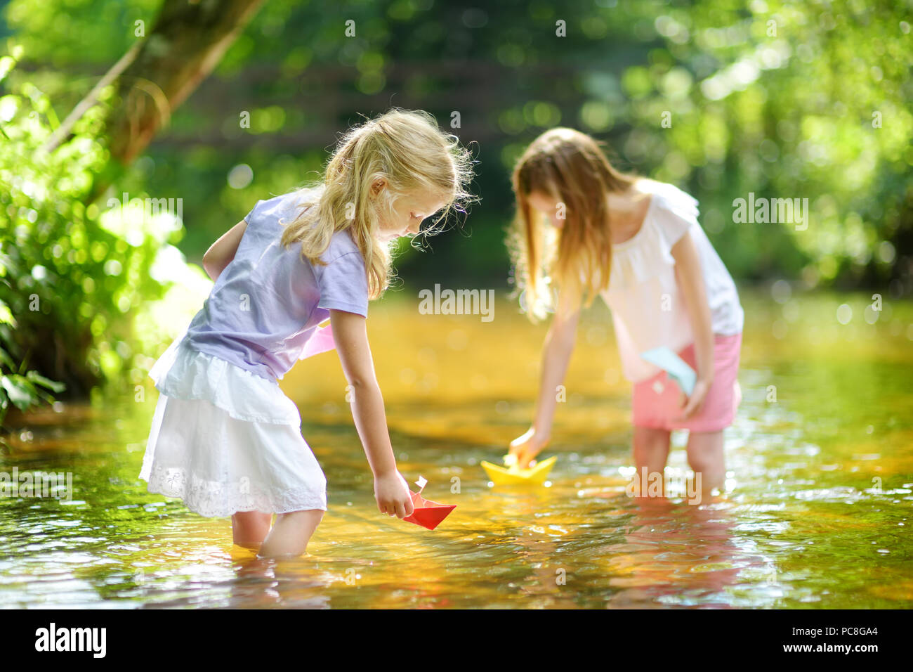 Zwei kleine Schwestern spielen mit Papier Boote durch einen Fluss an warmen und sonnigen Sommer. Kinder Spaß am Wasser. Aktivitäten im Sommer für kleine Zicklein Stockfoto