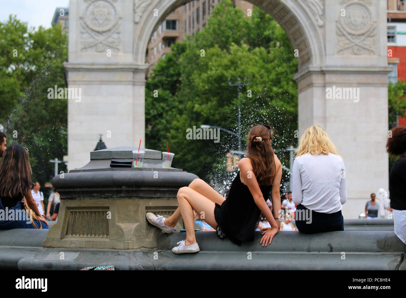 NEW YORK, NY - 10. Juli: Junge Frauen sitzen auf der Felge eines Washington Square Park Brunnen in Manhattan am 10. Juli 2017 in New York, USA. Stockfoto