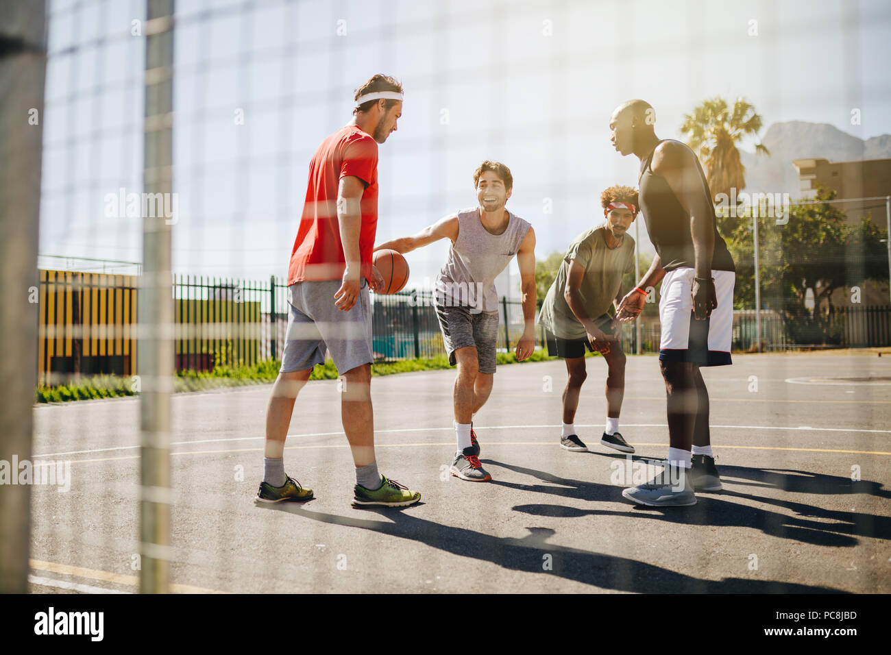 Vier Männer Basketball spielen in einem basketballplatz an einem sonnigen Tag. Männer üben Basketball Dribblings. Stockfoto