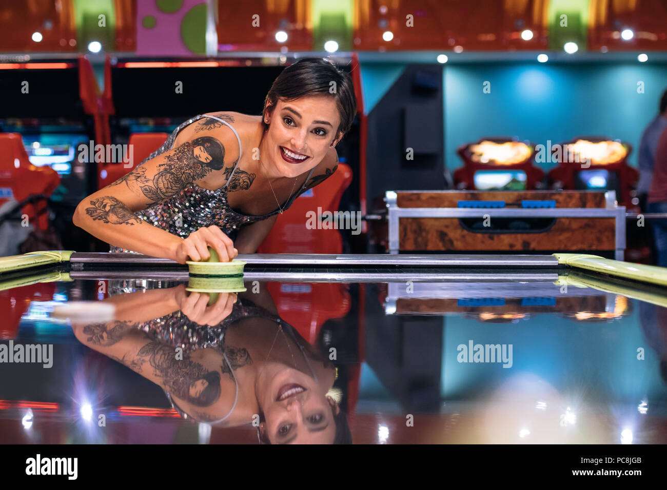 Lächelnde Frau mit einem Gaming arcade spielen Münze air hockey Spiel betrieben. Frau mit Spaß, das air hockey Spiel bei einem Gaming Salon. Stockfoto