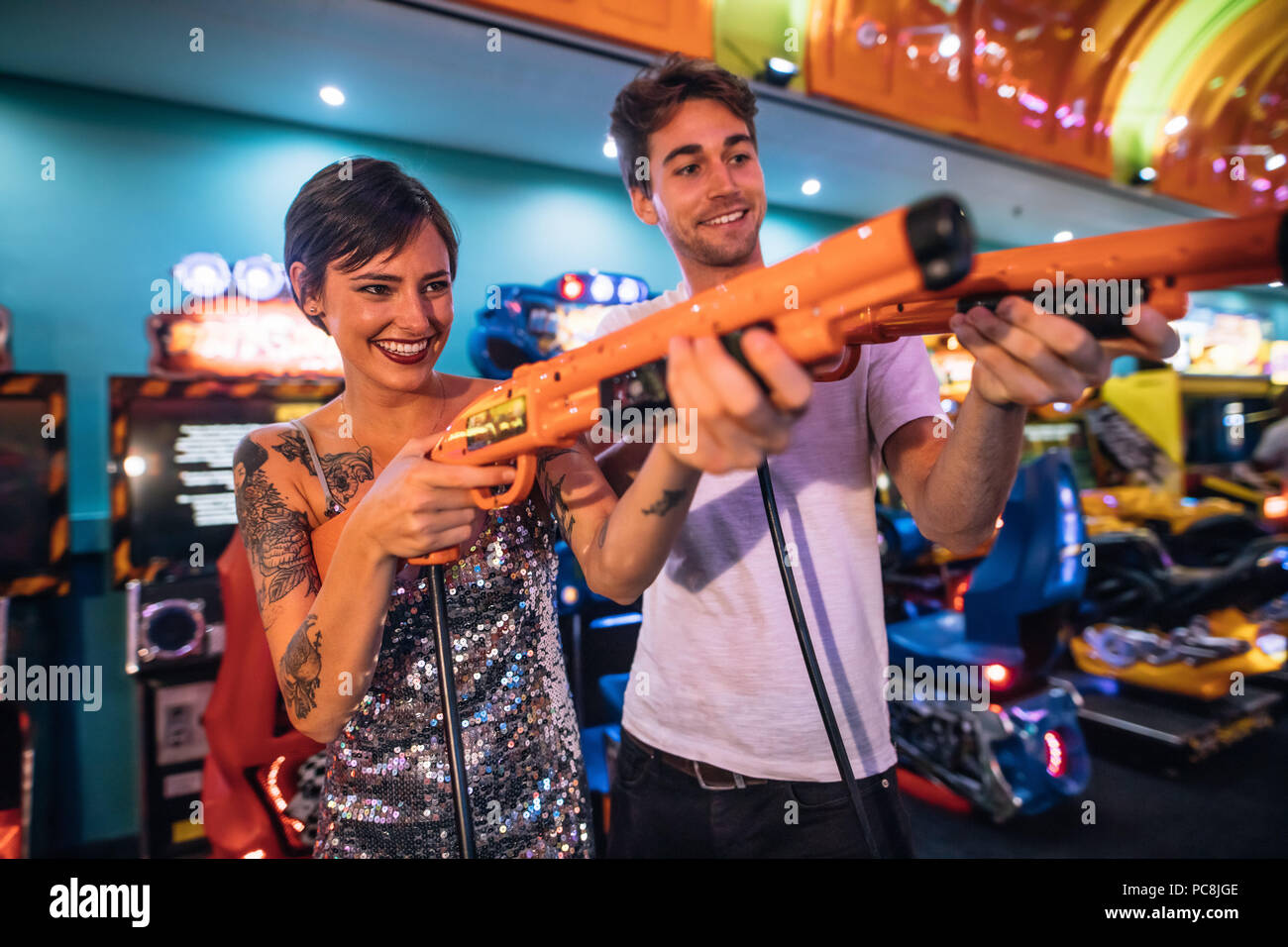 Glückliches Paar holding Elektrische gaming Waffen auf einem Gaming Salon. Mann und Frau spielen Spiele Spiele mit gaming Waffen auf einem Gaming Arcade. Stockfoto