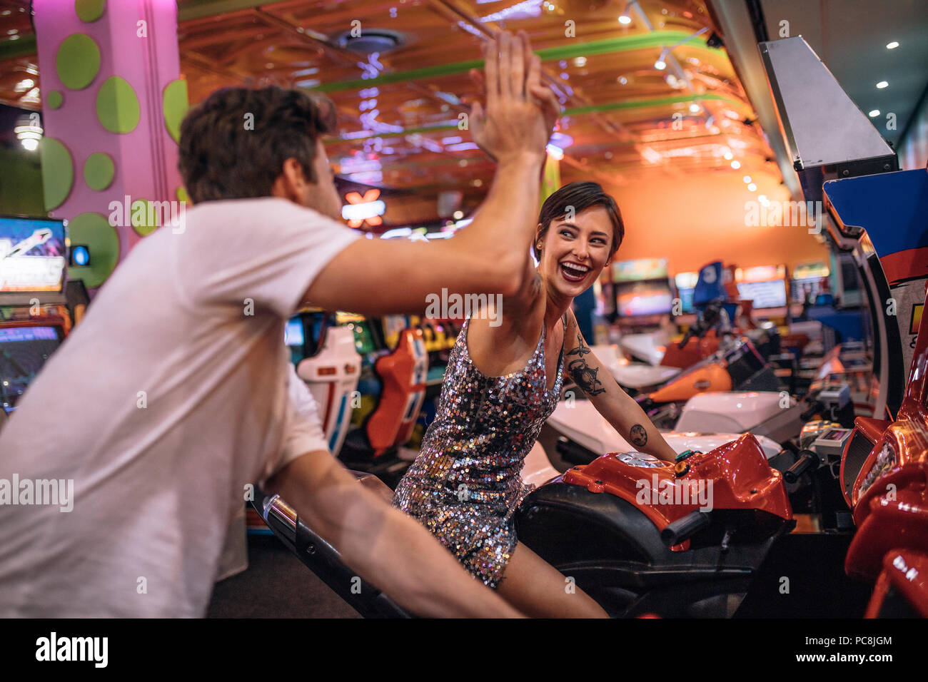 Die hohe fünf miteinander geben während des Spielens Bike Racing spiele Spiele Arcade. Paar beim Arcade racing Spiele bei einem Gaming Salon Stockfoto