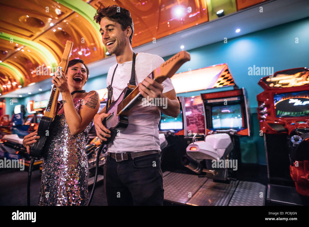 Paar Gitarre spielen Spiel Holding gaming Gitarren bei einem Gaming Salon. Lächelnd Mann und Frau Spaß Spiele spielen an einem Gaming Arcade. Stockfoto