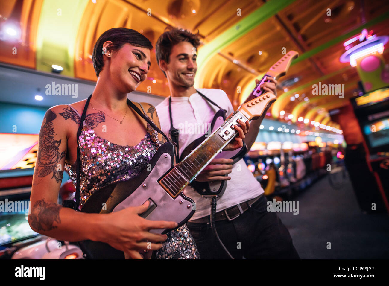Mann und Frau Holding gaming Gitarren spielen an einem Gaming Salon. Paar lustige Spiele spielen an einem Gaming Arcade. Stockfoto