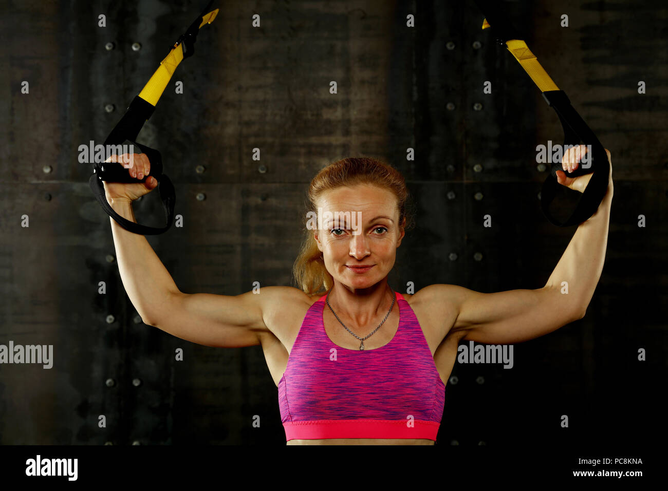 Einen jungen und mittleren Alter athletische Frau bei crossfit Schulung, Training mit TRX Suspension fitness Bänder über dunklen Hintergrund, Vorderansicht, Blick auf c Stockfoto