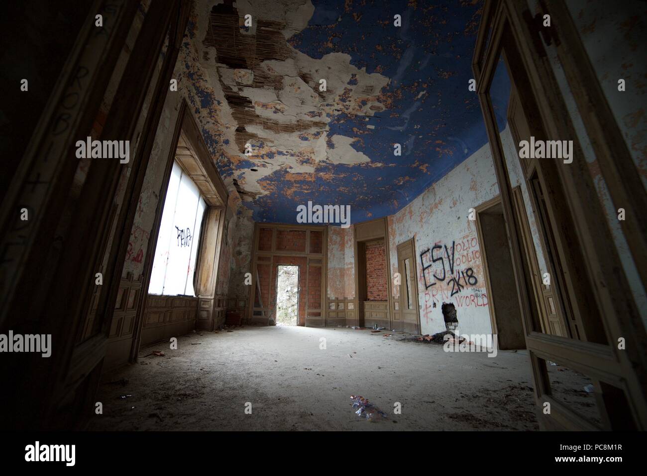Ein heruntergekommenes Zimmer in einem verlassenen Herrenhaus in Italien, mit Farbe blättert von den Wänden und viel Staub, Graffiti und Verfall. Stockfoto