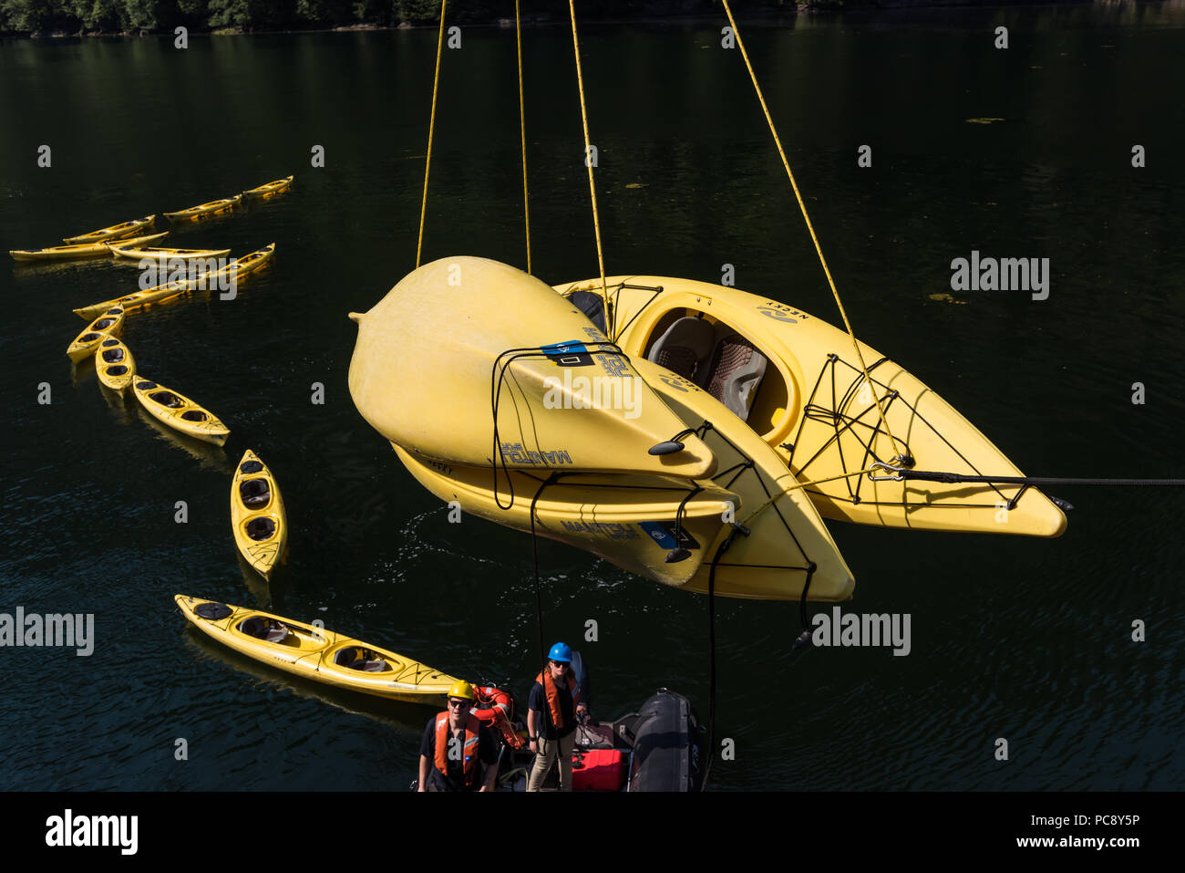 Zwei Besatzungsmitglieder des National Geographic Sea Bird überwachen die Senkung der 4 gelbe Kajaks mit anderen Kajaks im Wasser schwimmenden hinter Ihnen. Stockfoto