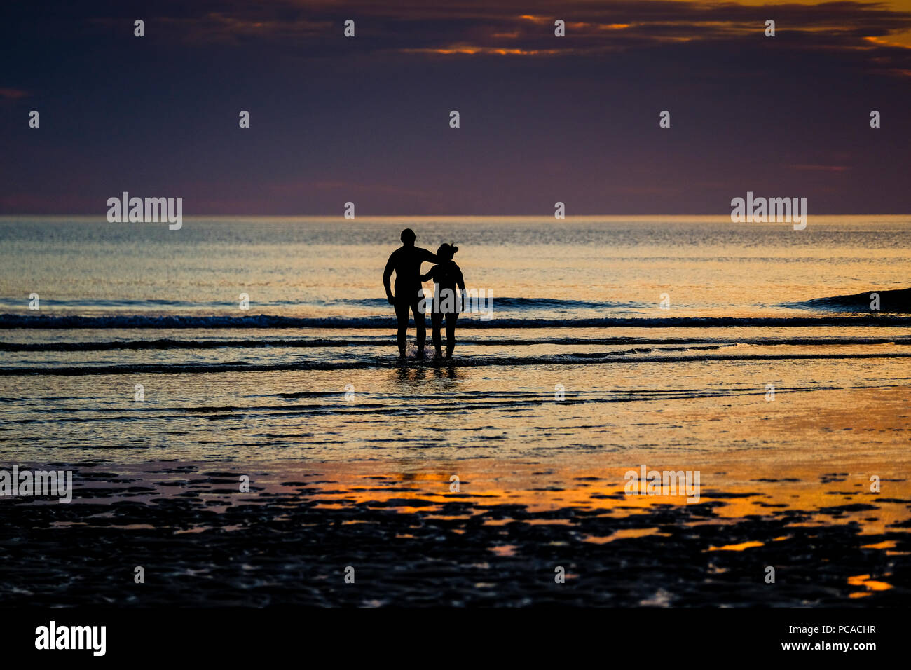Paar stehend auf Porth Strand in Newquay in Cornwall, mit Blick auf das Meer, wie die Sonne untergeht Stockfoto