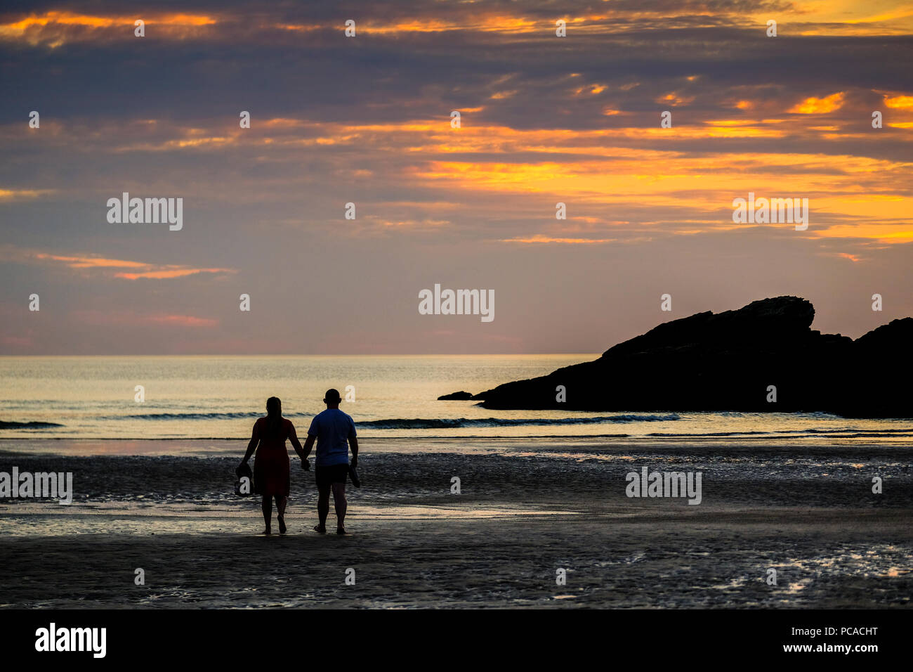 Paar stehend auf Porth Strand in Newquay in Cornwall, mit Blick auf das Meer, wie die Sonne untergeht Stockfoto