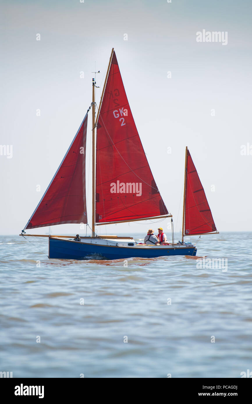 Eine rote Segelboot auf ruhiger See gesehen an einem warmen sonnigen Tag mit blauen Himmel. Stockfoto