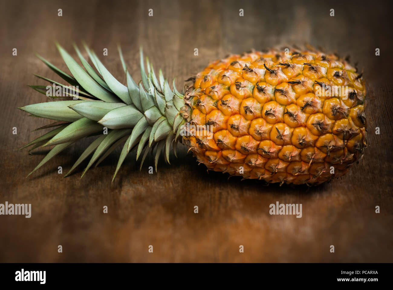 Single eine volle ganze Bio Ananas Obst auf hölzernen Hintergrund reifen Erwachsenen Reife, nach unten auf die Seite gelegt Stockfoto