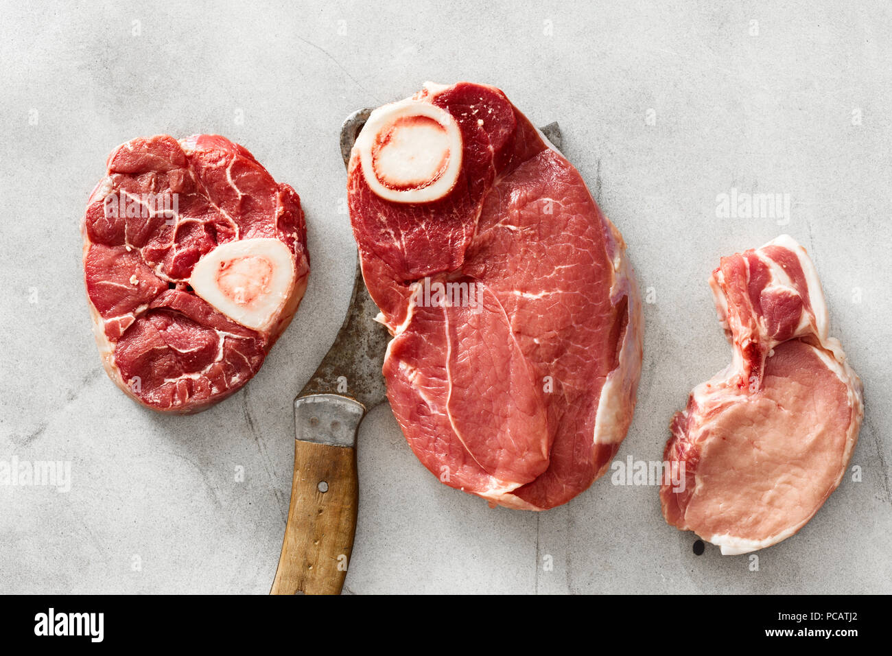 Stellen Sie rohes Rindfleisch Fleisch auf den Knochen- und Schweinefleisch auf weißem Beton Hintergrund mit fleischermesser, Ansicht von oben Stockfoto