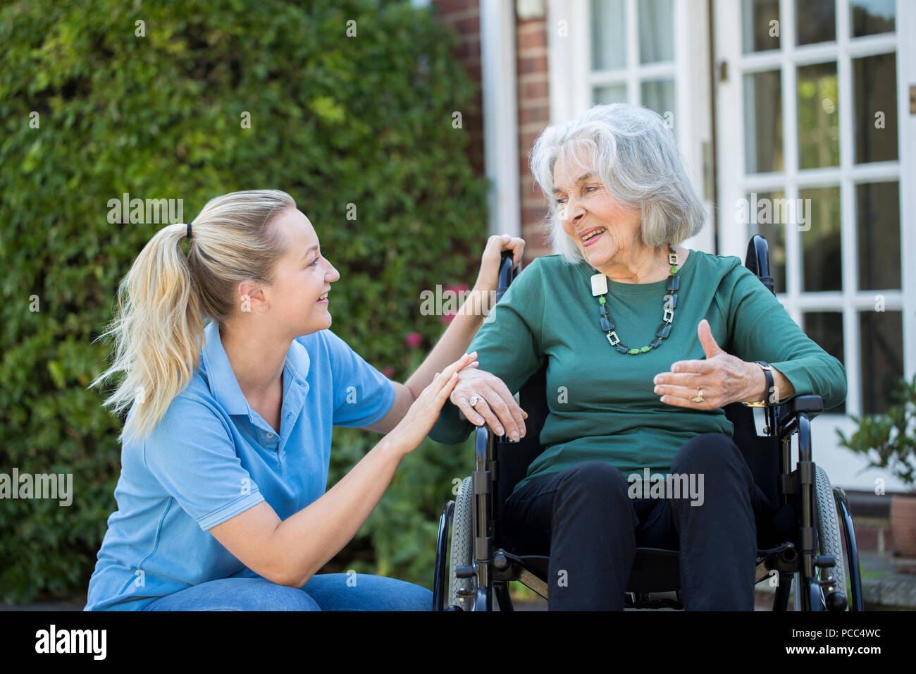 Pflegeperson Drücken ältere Frau im Rollstuhl außerhalb Home Stockfoto