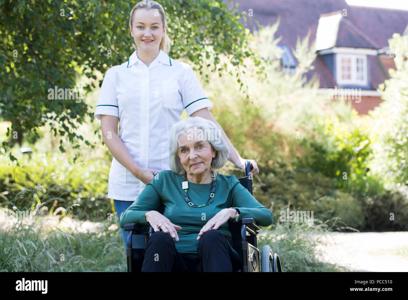 Portrait von pflegeperson Drücken ältere Frau im Rollstuhl außerhalb Home Stockfoto
