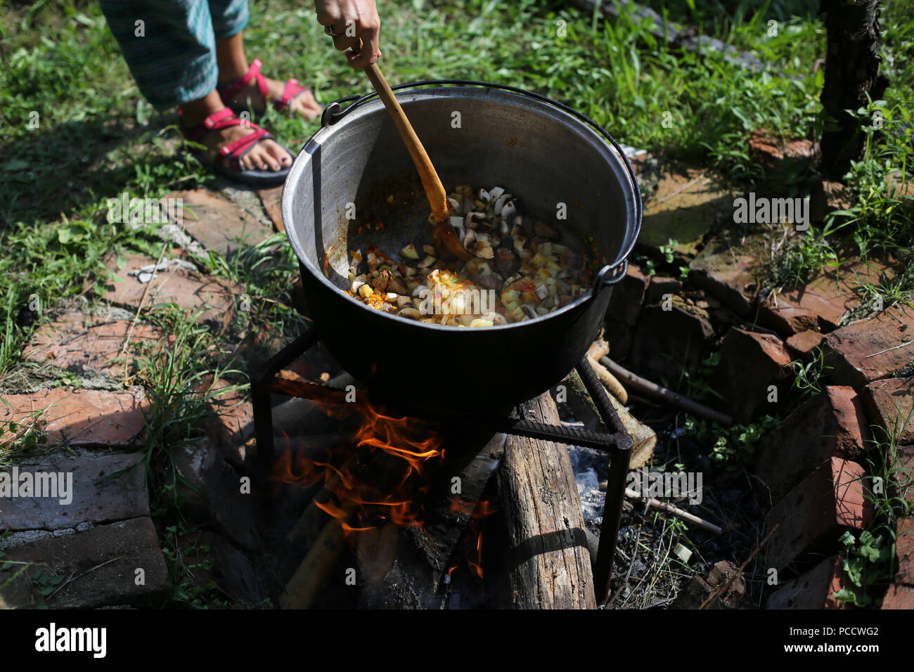 Frau Rühren in einer gusseisernen Kessel, wo ein gulasch Eintopf kocht, über offenem Feuer im Hinterhof eines ländlichen Haus in Rumänien anmelden Stockfoto