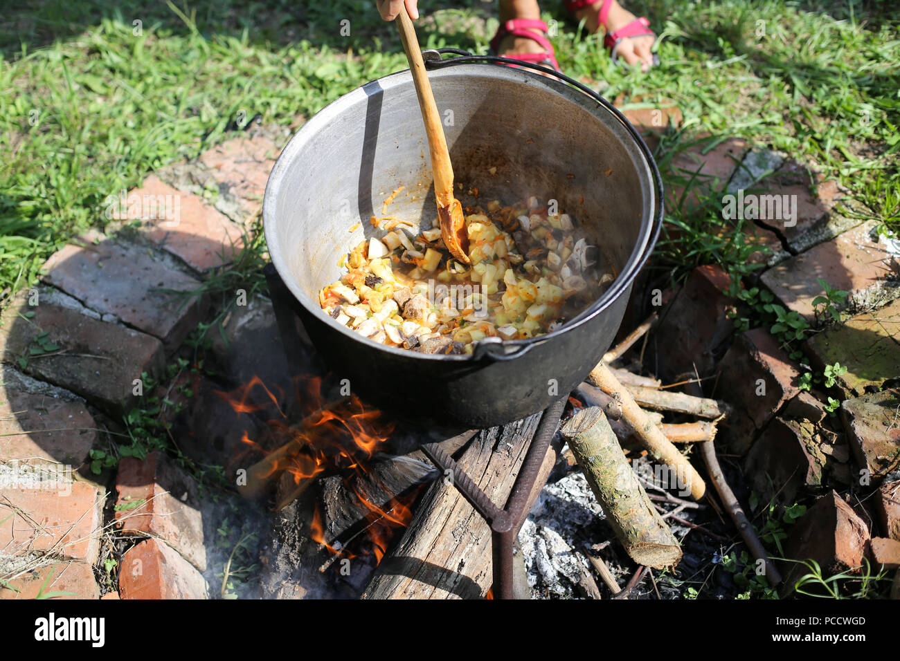 Frau Rühren in einer gusseisernen Kessel, wo ein gulasch Eintopf kocht, über offenem Feuer im Hinterhof eines ländlichen Haus in Rumänien anmelden Stockfoto