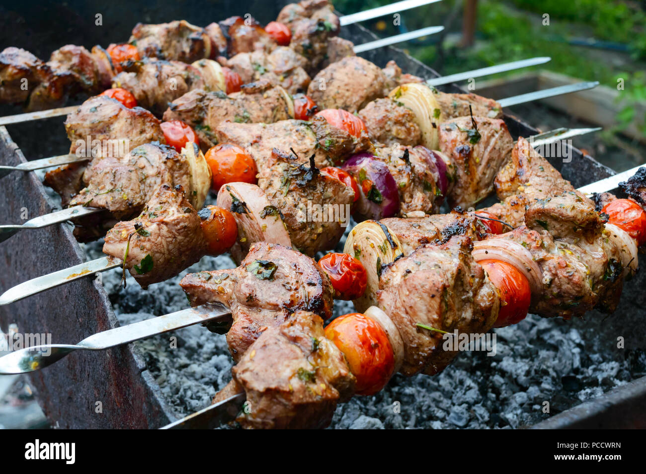 Saftige Shish Kebab aus Schweinefleisch, Tomaten am Spieß gebraten auf einem Feuer im Freien auf einem Hintergrund der Natur. Grill. Stockfoto