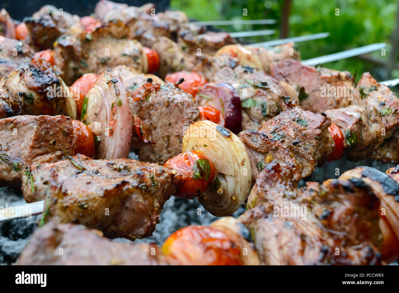 Saftige Shish Kebab aus Schweinefleisch, Tomaten am Spieß gebraten auf einem Feuer im Freien auf einem Hintergrund der Natur. Grill. Close-up Stockfoto