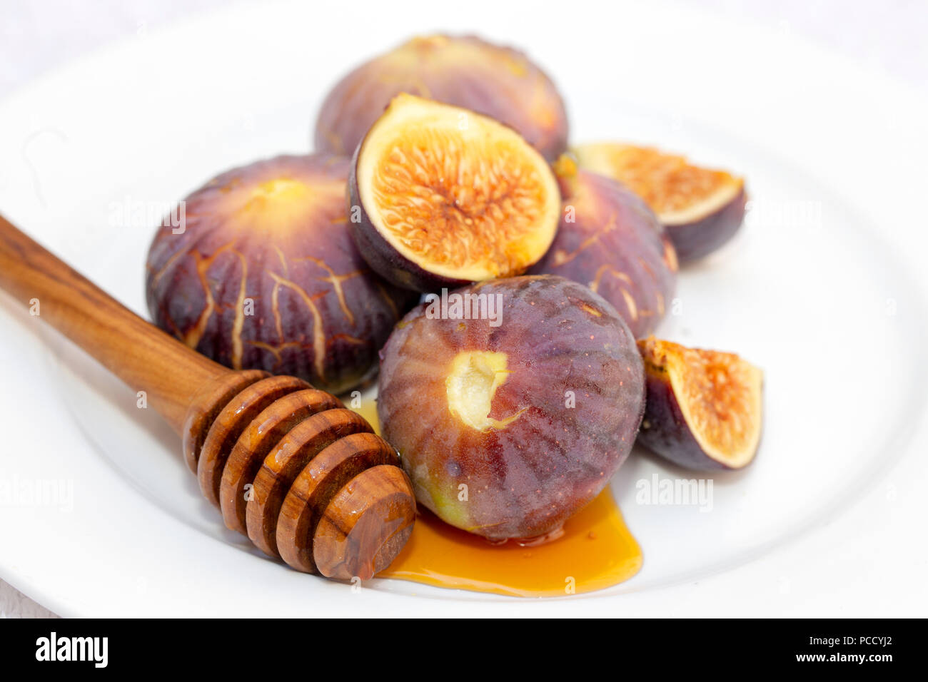 Ein Honig dropper Löffel mit Sirup und frischen süßen Feigen auf einem weißen Teller Stockfoto