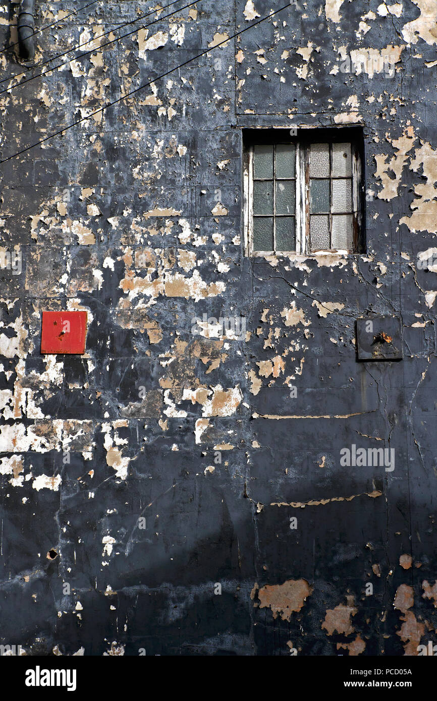 Eine helle rote Drehmomentstütze platte Kontraste anschaulich mit seiner schwarzen Nachbarn und abgenutzt und heruntergekommen Umgebung auf einem schäbigen und verwitterte Wand. Stockfoto